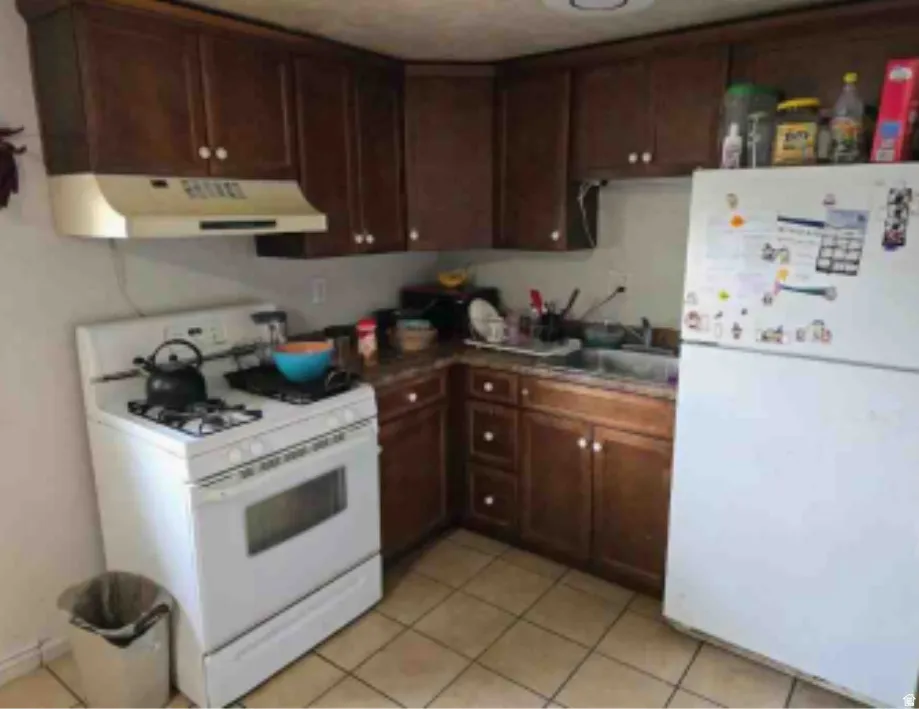 Kitchen featuring wood-finish cabinetry, tile flooring, white gas range, and a white refrigerator