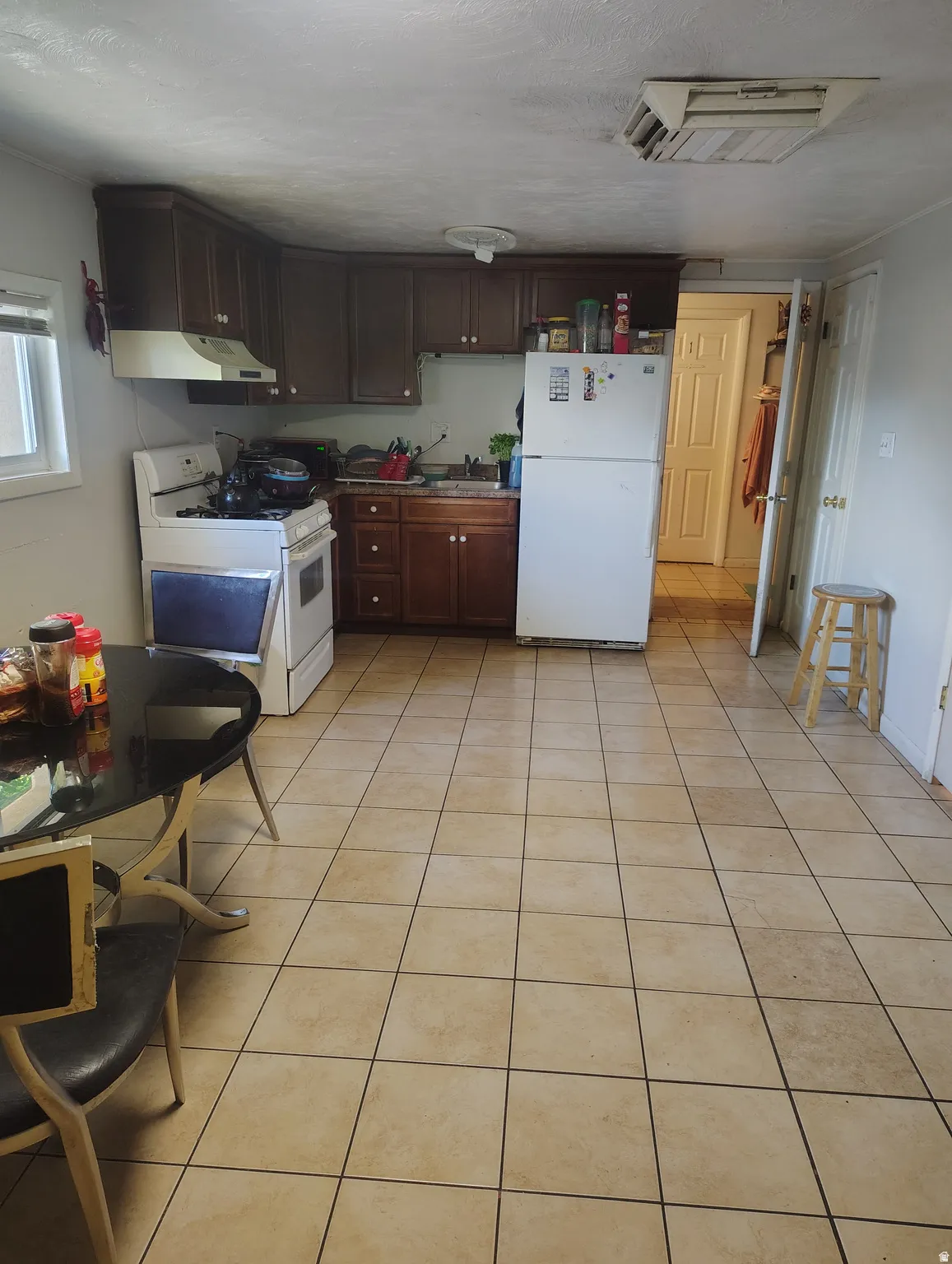Kitchen featuring an L-shaped cabinetry layout, overhead ventilation hood, window, and tile flooring