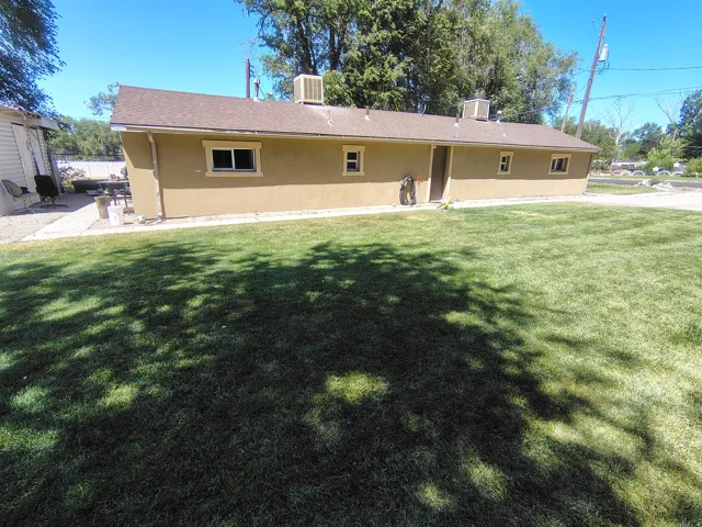Stucco exterior with multiple windows, a composite shingle roof, and a gravel patio area