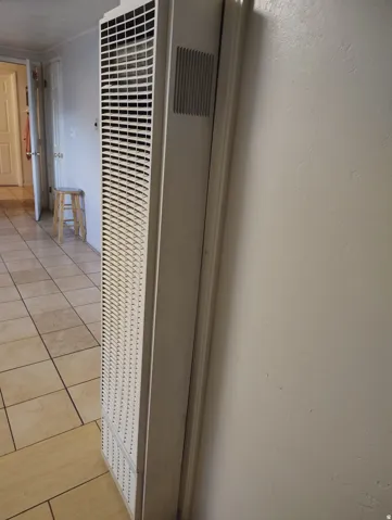 Wall-mounted heating unit with a louvered grille, integrated into a neutral wall with tile flooring