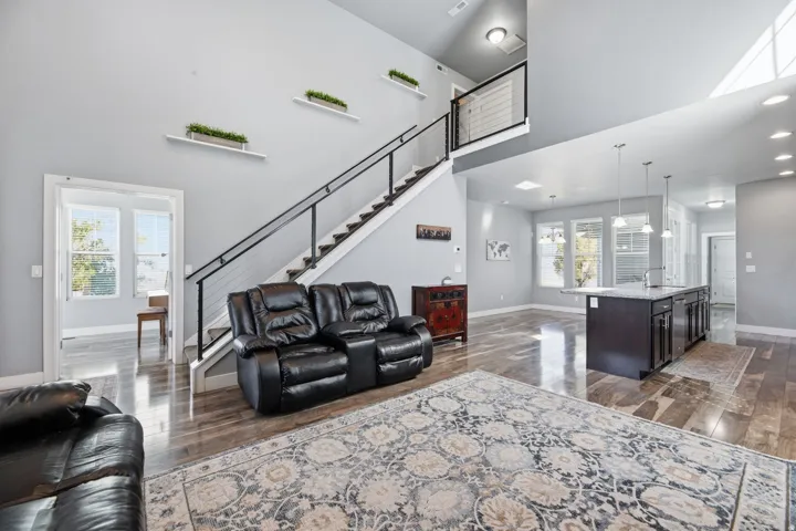 Open-concept living area featuring high ceilings, wood-finish flooring, a modern cable railing staircase, and recessed lighting