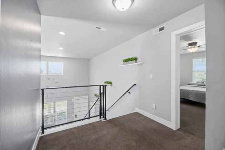 Modern loft-style landing featuring dark wood-finish flooring, white walls, and contemporary metal railing with horizontal cable design