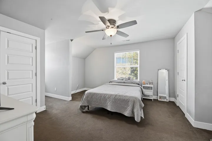 Spacious room featuring neutral paint, brown carpeting, a window with blinds, a ceiling fan with integrated lighting, and white paneled doors