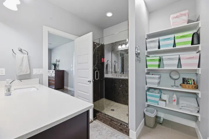 Spacious bathroom with a white countertop vanity, glass-enclosed shower, and built-in shelving
