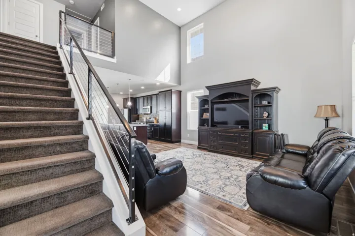 Two-story great room with high ceilings, wood-finish flooring, and a carpeted staircase with a modern cable railing