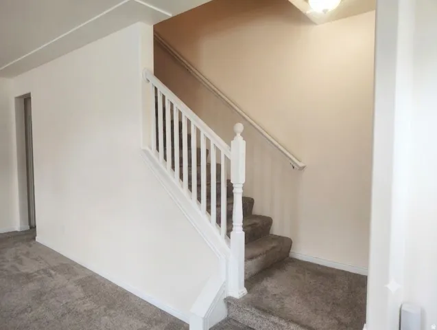 Staircase featuring white balusters and handrail, neutral-toned walls, and carpeted steps