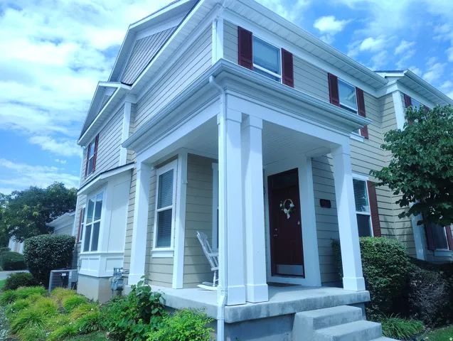 Multi-level residence featuring a covered front porch with white columns, concrete steps, a dark-toned entry door, and red shutters accenting upper-level windows