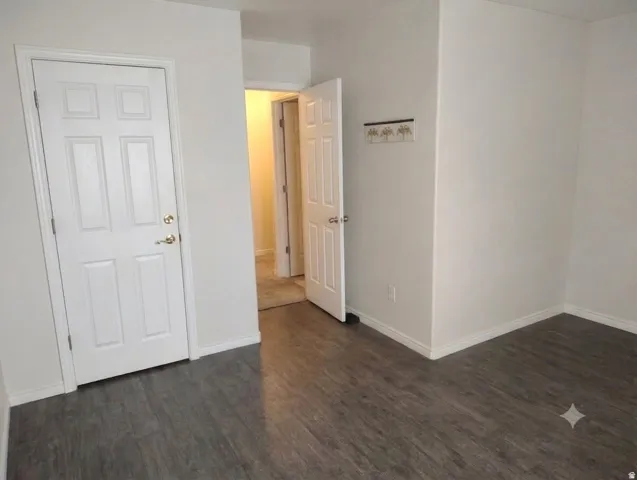 Wood-finish flooring with white baseboards, a six-panel interior door with brass hardware, and white walls