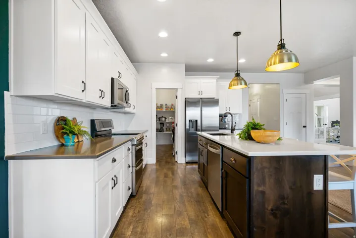 White shaker cabinetry, stainless steel appliances, wood-finish flooring, central island with seating, and recessed lighting
