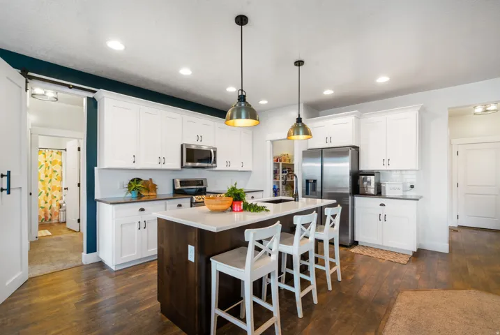 Kitchen featuring white cabinetry, wood-finish flooring, a central island with countertop seating, stainless steel appliances, and recessed lighting