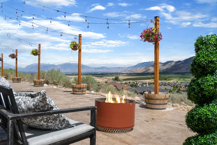 Expansive outdoor patio with string lighting, a fire pit, and hanging floral arrangements on wooden posts
