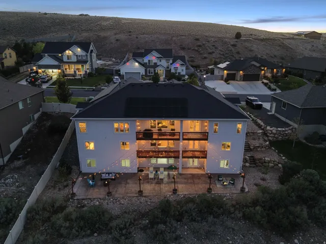 Multi-level dwelling with a dark shingled roof, multiple balconies, a lower-level patio, and exterior lighting