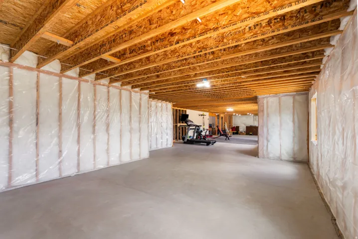 Expansive unfinished basement featuring concrete flooring, exposed wood joists, and insulated framed walls