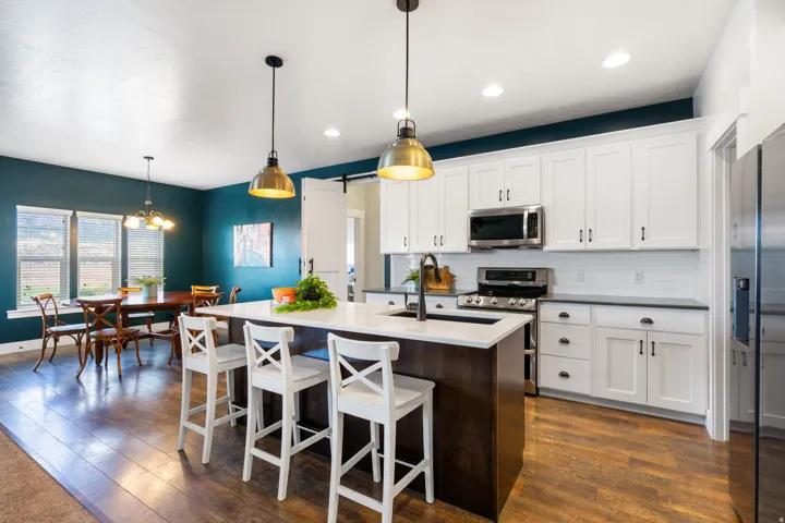 Argon gas filled windows, Open-concept kitchen with a central island, white shaker-style cabinetry, wood-finish flooring, stainless steel appliances, and pendant lighting