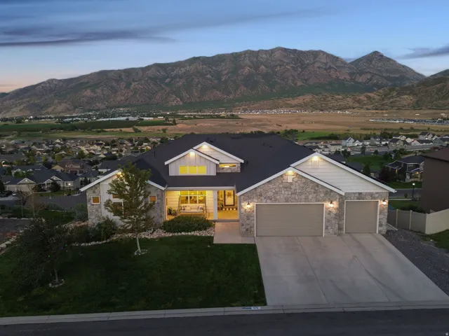 Stone facade exterior with a two-car garage, covered entry porch, dark shingle roof, and a prominent mountain backdrop