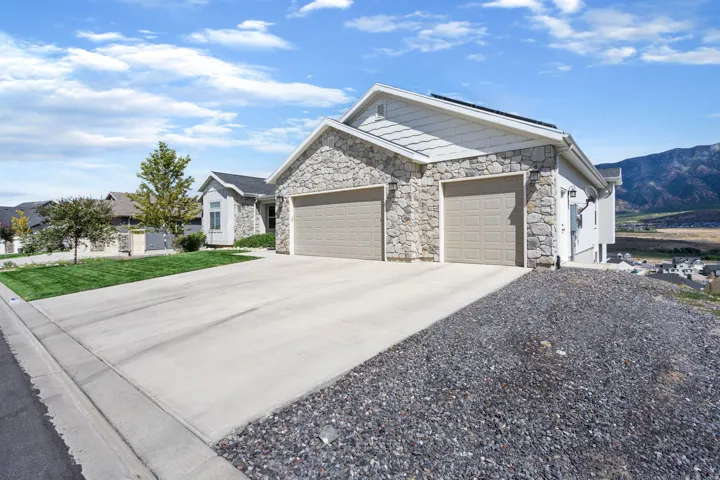 Stone facade and siding exterior featuring a 3-car garage with panel doors, a concrete driveway, and a sloped gravel landscaping area