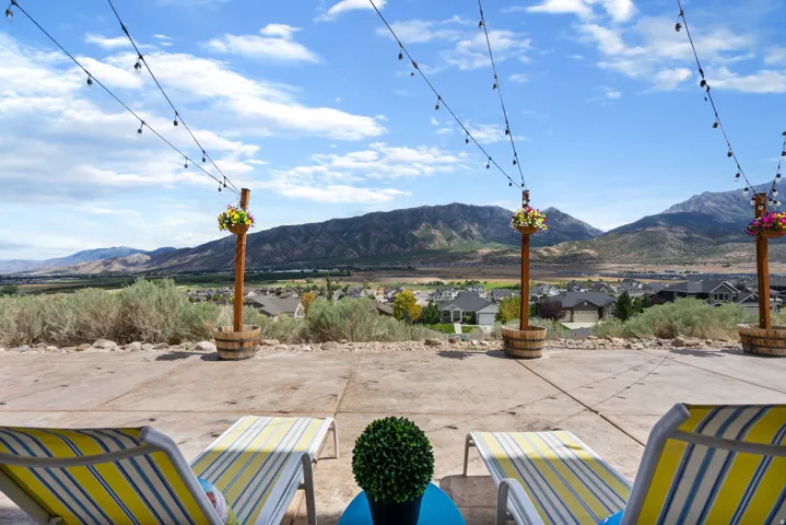 Expansive concrete patio with string lights, barrel planters, and mountain scenery