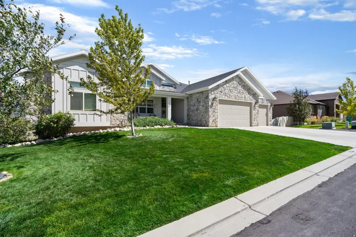 Stone facade detailing, attached 3-car garage, expansive green lawn, mature landscaping, and light-colored siding