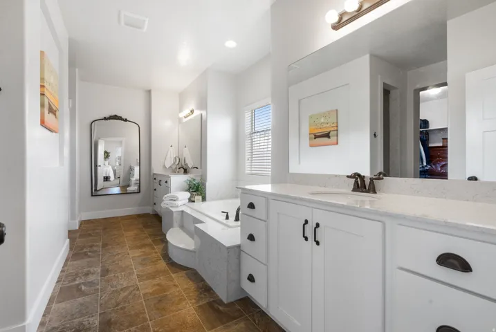 Dual vanity with white cabinetry and light-colored countertops, built-in soaking tub with steps, and tile flooring