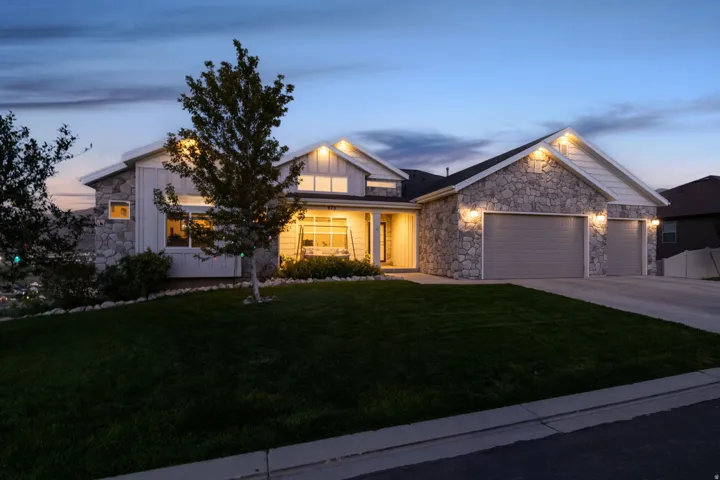 Stone facade with board and batten accents, attached multi-car garage, manicured lawn, paved driveway, and covered front entry