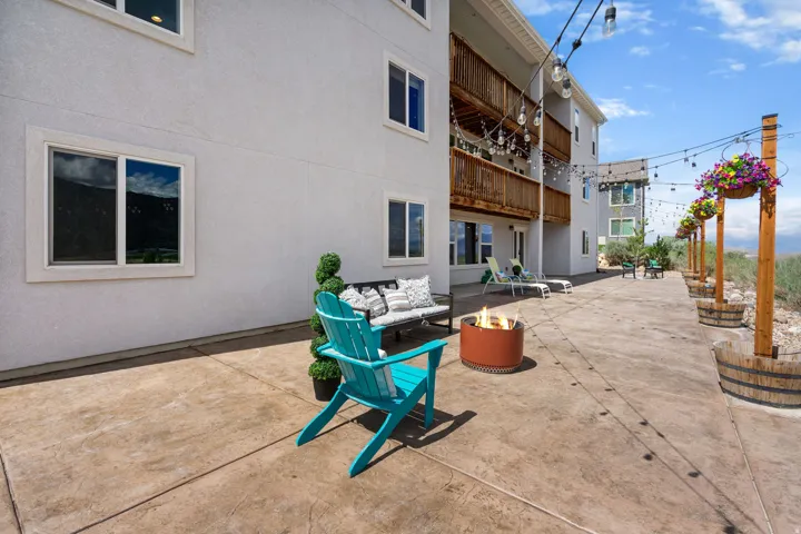 Ground-level patio with stamped concrete, string lighting, and multiple balconies featuring wood railings