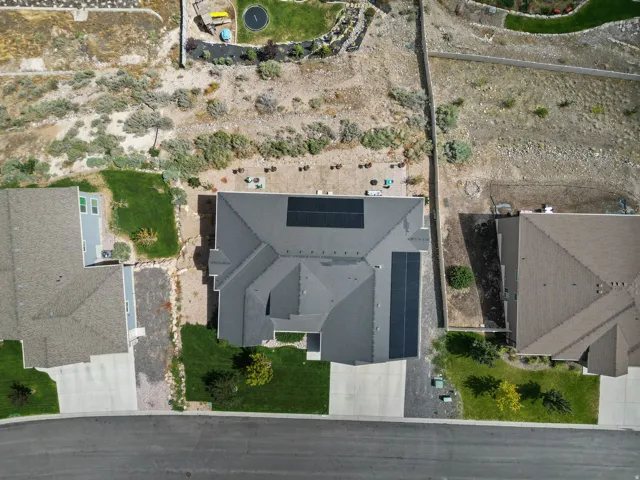 Gabled roofline with solar panel installation, paved driveway, and established lawn