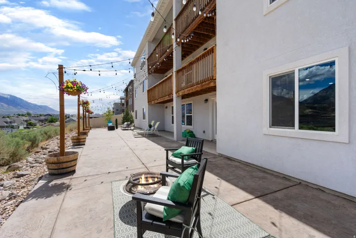 Expansive concrete patio with string lighting, a built-in fire pit, and upper-level balconies with wood railings