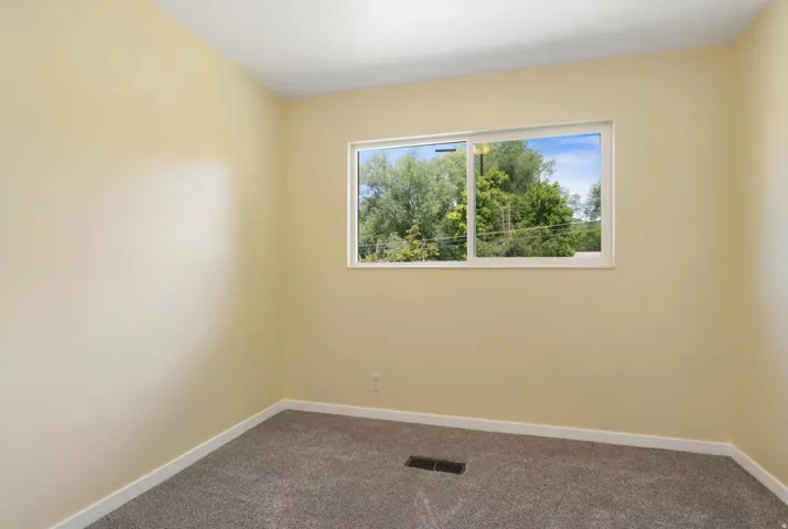 Neutral wall paint, gray carpet flooring, white window trim, and a window with outdoor scenery