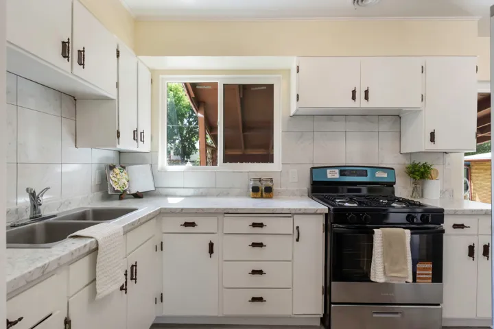 Bright kitchen featuring crisp white cabinetry with black hardware, white subway tile backsplash, and stainless steel appliances including a black gas range