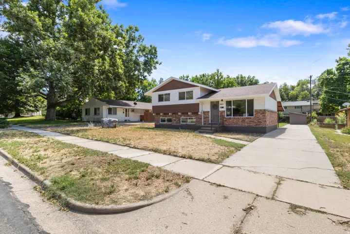 Split-level residence featuring a brick and white siding exterior, an attached concrete driveway, and mature trees providing shade