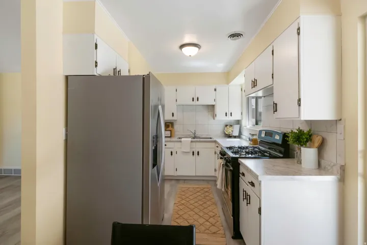 Kitchen featuring white cabinetry, stainless steel refrigerator, dark gas range, and stone-finish countertops with a tile backsplash