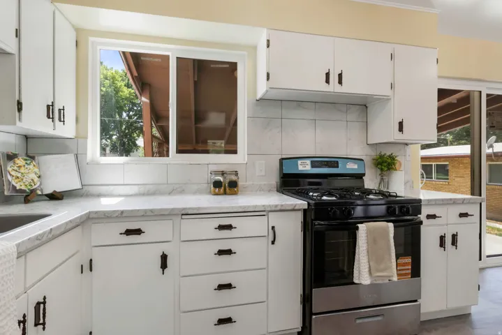 White cabinetry with dark hardware, stone-finish countertops, tile backsplash, and a stainless steel and black range