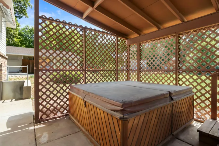 Covered patio featuring a hot tub with wood-finish siding, latticework screening, and a concrete pad