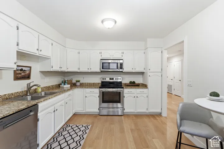 White cabinetry, stainless steel appliances, light wood-finish flooring, and speckled countertops