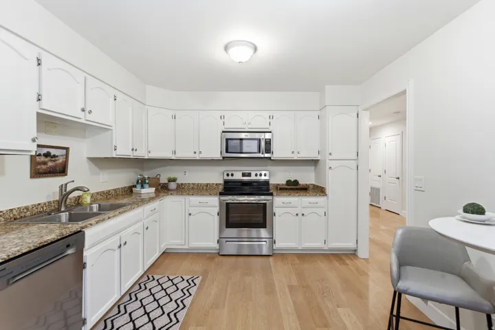 White cabinetry, stainless steel appliances, light wood-finish flooring, and speckled countertops