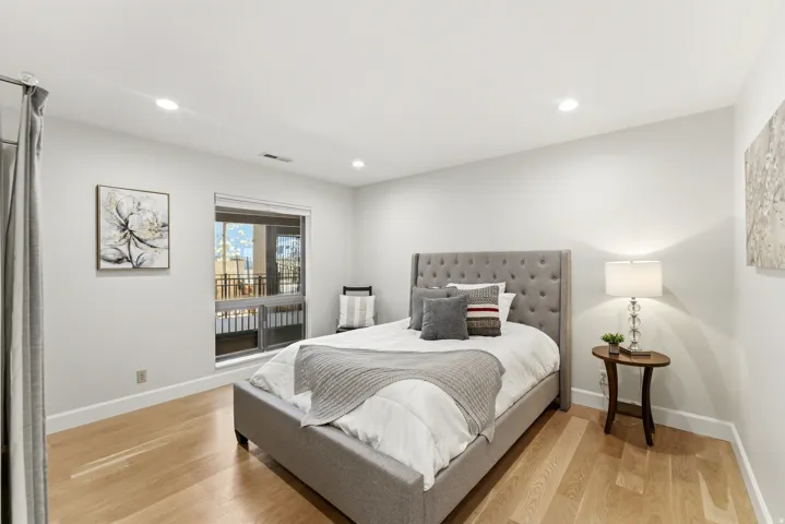 Recessed ceiling lighting, wood-finish flooring, large window with balcony access, and white wall finishes