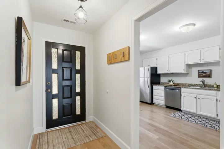 Entryway featuring a black door with frosted glass panels, wood-finish flooring, and an open archway to the kitchen