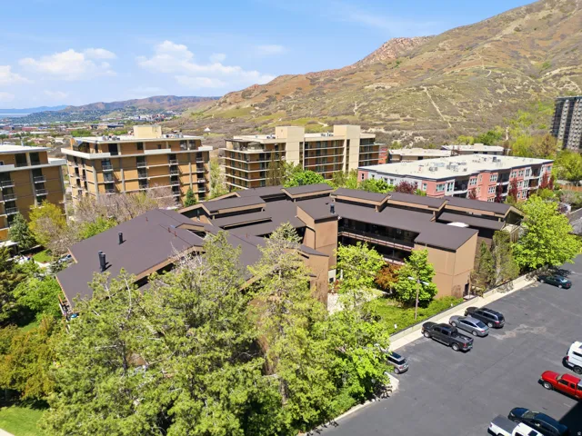 Multi-story building with brown exterior and dark sloped roofs, surrounded by mature trees