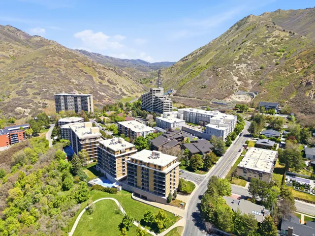 Modern residential community nestled in a verdant valley, featuring contemporary multi-story apartment buildings with clean architectural lines, expansive manicured green spaces with mature landscaping, and surrounding hillside terrain with natural vegeta