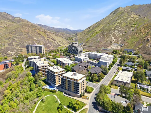 Modern residential community nestled in a verdant valley, featuring contemporary multi-story apartment buildings with clean architectural lines, expansive manicured green spaces with mature landscaping, and surrounding hillside terrain with natural vegeta