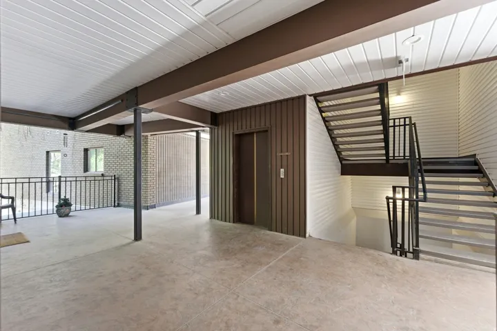 Covered outdoor corridor with concrete flooring, elevator access, and a multi-level staircase with metal railings