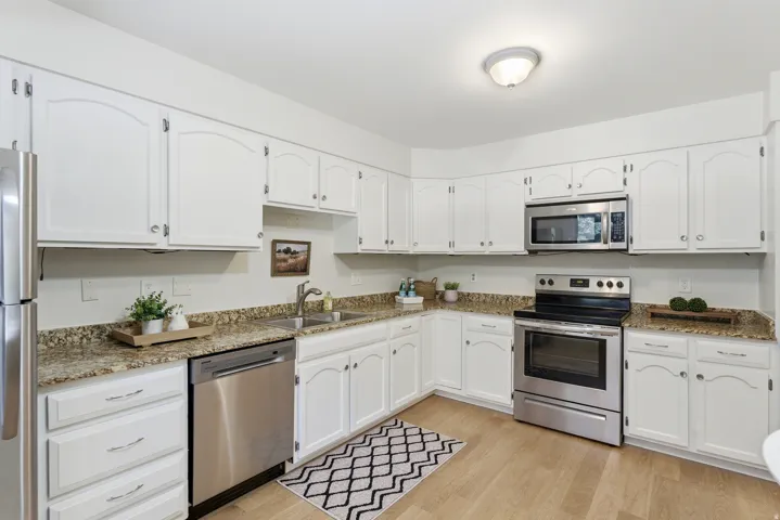 White cabinetry, granite-finish countertops, stainless steel appliances, wood-finish flooring, and recessed lighting