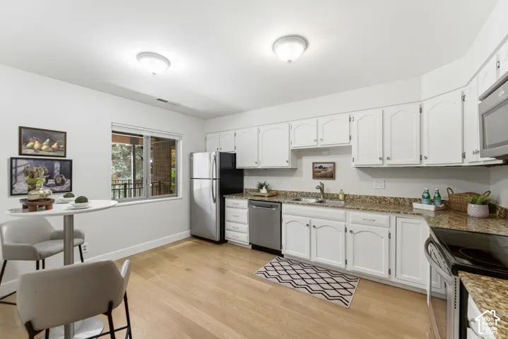 Kitchen featuring wood-finish flooring, white cabinetry, a built-in microwave, and stainless steel appliances