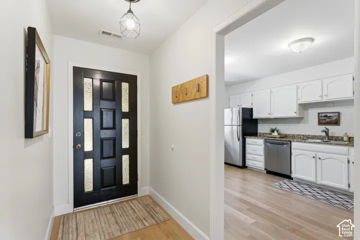 Entryway featuring a black door with frosted glass panels, wood-finish flooring, and an open archway to the kitchen