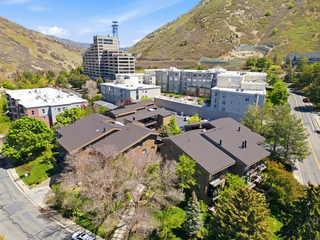 Modern residential community nestled in a verdant valley, featuring contemporary low-rise apartment buildings with clean architectural lines, expansive manicured grounds with mature landscaping, and dark-finish roofing