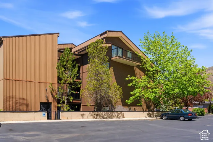 Multi-story building featuring brick and vertical panel siding, multiple balconies with black railings, and an asphalt parking area