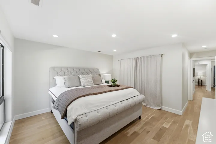 Recessed ceiling lighting, wood-finish flooring, white walls, and a large window with privacy shades