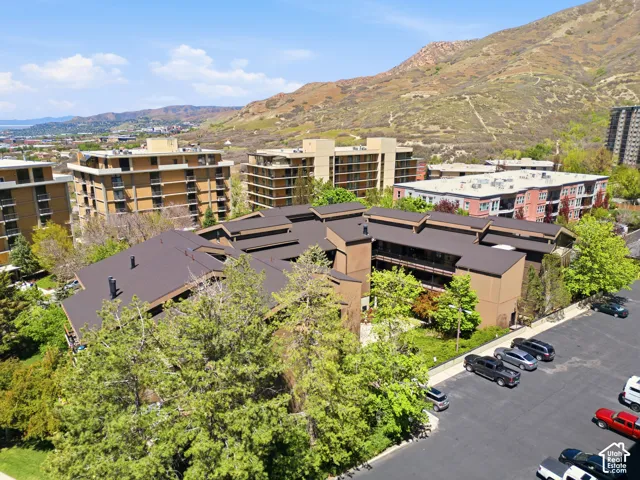 Multi-story building with brown exterior and dark sloped roofs, surrounded by mature trees