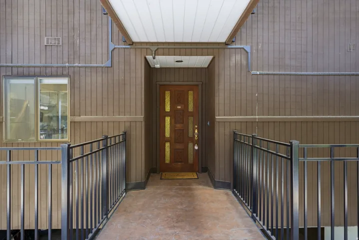 Wood-paneled exterior featuring a covered entryway, a decorative wood front door with brass accents, and a window with a neutral frame