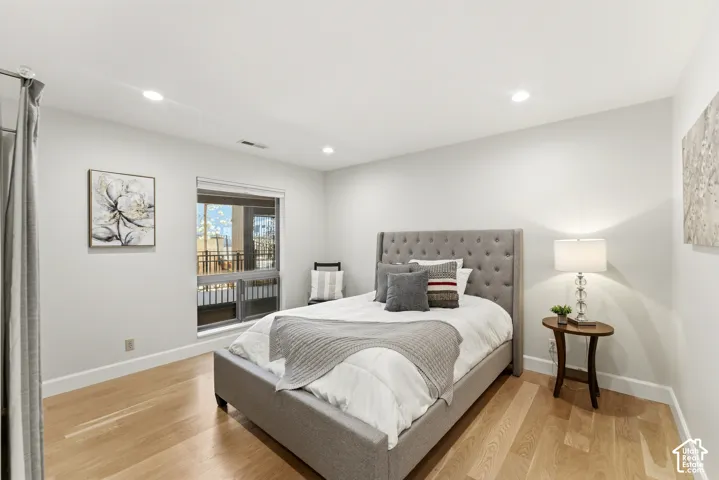 Recessed ceiling lighting, wood-finish flooring, large window with balcony access, and white wall finishes